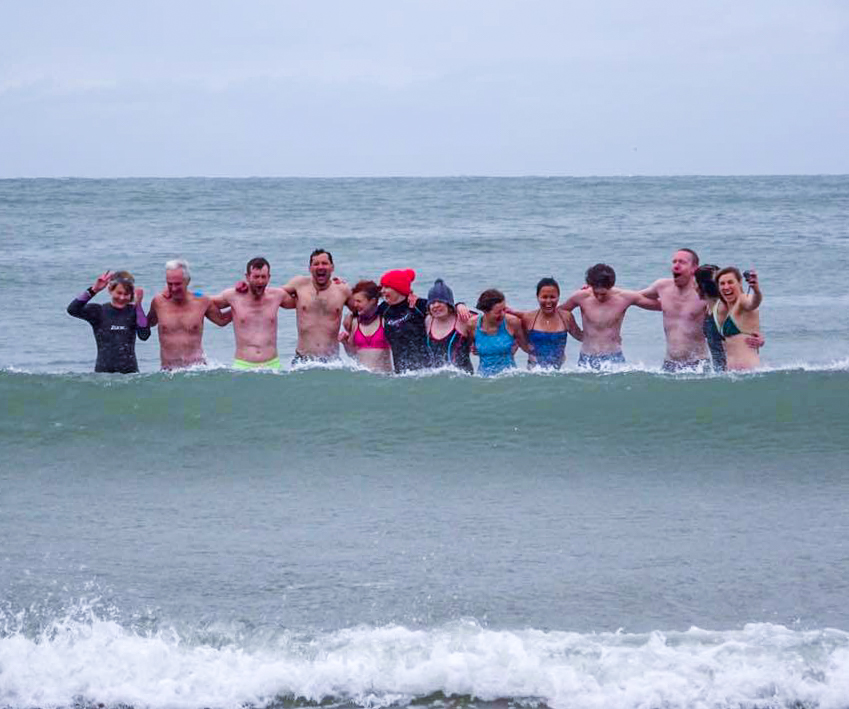 Wave breaks in front of cold swimmers